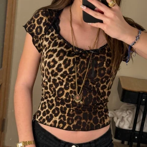 Leopardmönstrad topp med spetsdetaljer - Trendig leopardmönstrad topp med korta ärmar och en söt rosett framtill. Toppen har spetsdetaljer vid halsringningen.❤️St S!