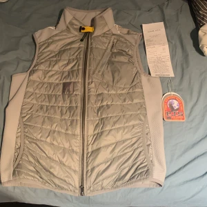 Grå quiltad väst från Parajumpers - Säljer en snygg grå quiltad väst från Parajumpers. Västen har en dragkedja framtill och en hög krage. Den är perfekt för lager-på-lager och har en sportig look med praktiska fickor. Säljer den för 2000kr pga den är lagad med fel färg. Köpte den från Room 1006 för 3000kr, har använt den en del men det mesta är defekt fritt. Pris kan diskuteras!
