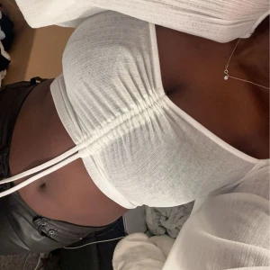 Vit ribbad topp - Säljer en snygg vit ribbad topp med knytning framtill. Toppen är croppad och har en tight passform som framhäver figuren. Perfekt för studenten eller sommar. Från Nelly. Aldrig andvänt.