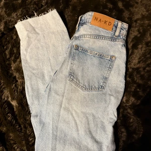 Ljusblå jeans från NA-KD - Snygga ljusblå jeans från NA-KD med en klassisk femficksdesign och råa kanter vid bensluten. Perfekta för en avslappnad stil. Märkeslapp i brunt läder baktill.