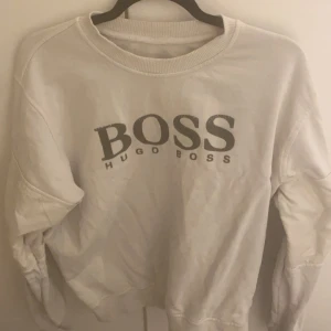 Vit sweatshirt från Hugo Boss - Säljer en stilren vit sweatshirt från Hugo Boss med deras ikoniska logga tryckt på framsidan. Tröjan har långa ärmar och en klassisk rund halsringning. Perfekt för en avslappnad och trendig look.