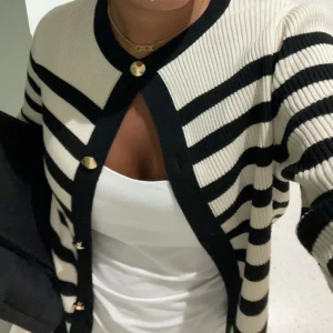 Randig kofta med knappar - Snygg randig kofta i svart och vit med ribbad struktur. Den har långa ärmar och knappar framtill. Perfekt för en stilren look.