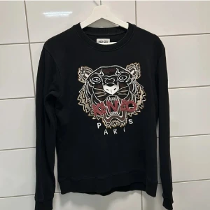 Kenzo tröja - Säljer en svart sweatshirt från Kenzo med ett stort broderat tigerhuvud och texten 'Kenzo Paris' på framsidan. Tröjan har långa ärmar och rund halsringning. Pris kan diskuteras!