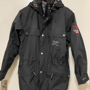Svart jacka från Peak Performance - Säljer en svart jacka från Peak Performance i GORE-TEX-material. Jackan har en huva, dragkedja och knappar framtill samt flera praktiska fickor. Perfekt för utomhusaktiviteter med stil. Jackan är retro, inte mycket använd. Har även en avtagbar fleeceväst inuti. Så du får två kvalitéts plagg till priset av ett.