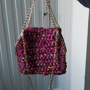 Färgglad virkad väska med kedjor - Säljer en unik och färgglad virkad väska med guldiga kedjor. Väskan har en härlig mix av färger som rosa, blå och lila, vilket ger den ett livfullt utseende. Perfekt för att liva upp vilken outfit som helst!