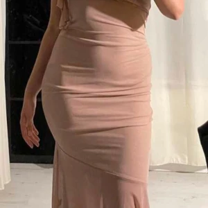 Klänning  - En vacker klänning i en mjuk rosa färg med en elegant silhuett. Klänningen har en spetsad design vid axlarna och en flödande kjol. Den är perfekt för en festlig tillställning eller en romantisk kväll.passar även S
