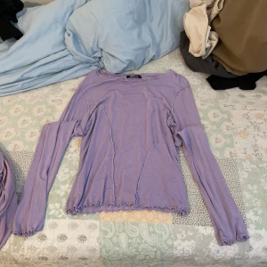 Ljuslila långärmad topp - Säljer en superfin ljuslila topp med långa ärmar. Den har en unik design med vågiga kanter och sömmar som ger en cool look. Perfekt för både vardag och fest! 💜