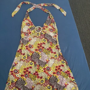 Färgglad blommig klänning från Mode Italy - Säljer en superfin och färgglad klänning från Mode Italy. Den har ett blommigt mönster i rött, gult, svart och vitt. Klänningen är ärmlös och har en snygg ringdetalj framtill. Perfekt för sommarens fester eller en dag på stan!