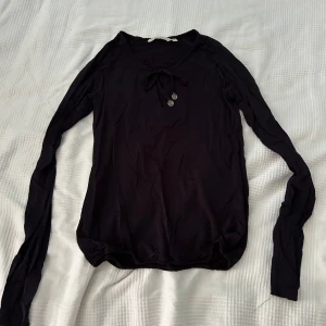 Svart långärmad tröja från House of Lola - Säljer en stilren svart långärmad tröja från House of Lola. Tröjan har en söt knytning vid halsen och två dekorativa knappar framtill på snörena. 