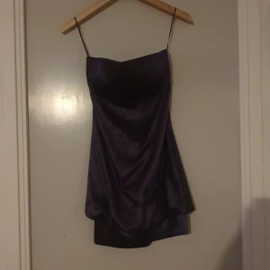 Lila axelbandslös klänning - Säljer en elegant lila klänning utan axelband. Den är gjord i ett glansigt material som ser ut som satin och har en figurnära passform. Perfekt för festliga tillfällen!