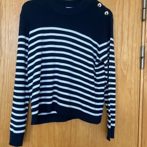 Randig tröja - Jättefin stickad randig vit blå tjocktröja från kapphal. Guldknappar längs ena axeln. Kontakta gärna för fler frågor och prisförslag