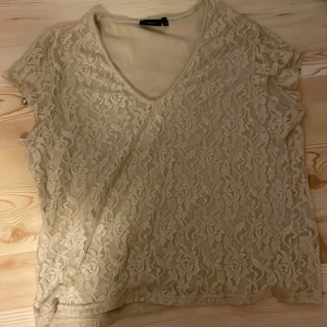 Beige spetsblus från H&M - Säljer en superfin beige spetsblus från Lindex. Den har en v-ringad hals och korta ärmar. Perfekt för både vardag och fest! 💫