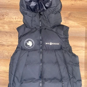 Sail Racing Arctic Down Vest - Säljer en svart dunväst från Sail Racing. Västen har en dragkedja framtill och en praktisk huva. Den är perfekt för kyliga dagar och har en stilren design med logotypdetaljer. Passar bra för både höst och vinter. Nypris 3500, skick 10/10