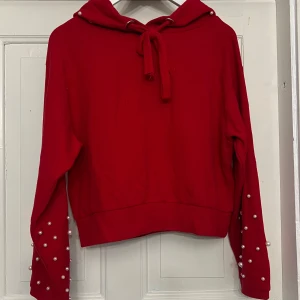Röd hoodie med pärldetaljer - Säljer en röd hoodie med pärlor på ärmarna och luvan. Köpt från Chiquelle och är i storlek 38. 