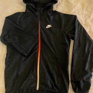 Vintage nikejacka - Vintage svart NIKE jacka med rödfärgad dragkedja och huva i strl S. Det är en tunn vindjacka i fint skick bortsett från ett litet hål vid höger ficka men inget man tänker på vid användning. Normal i storlek, köparen står för frakten💞