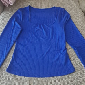 Blå ribbad topp - Säljer en snygg blå ribbad topp med långärmade ärmar. Den har en fyrkantig halsringning som ger en stilren look. Oanänd! 100% nytt. 