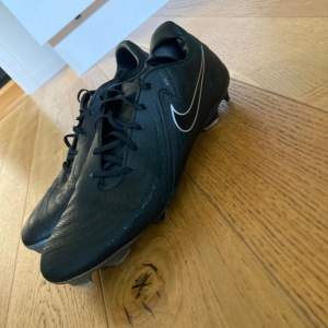 Säljer ett par svarta Nike fotbollsskor i jättebra skick bara använt ett par gånger. De har äkta fjäll och är gjorda i ett slitstarkt material, regntäta och har snörning för en säker passform. Perfekta för fotbollsträning! 