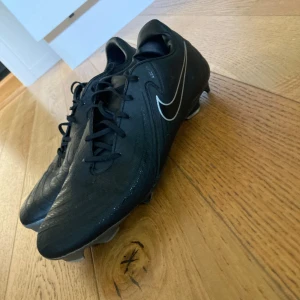 Svarta Nike fotbollsskor - Säljer ett par svarta Nike fotbollsskor i jättebra skick bara använt ett par gånger. De har äkta fjäll och är gjorda i ett slitstarkt material, regntäta och har snörning för en säker passform. Perfekta för fotbollsträning! 