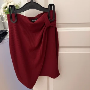 Röd kjol från Boohoo - Säljer en superfin röd kjol från Boohoo. Den har en snygg omlott-design och är ribbad vilket ger en cool textur. Perfekt för både fest och vardag! 🥰