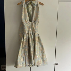 Asos Luxe blå klänning, storlek M - En vacker klänning med en halterneck och en rosett i nacken från Asos Luxe i storlek M. Klänningen har ett blommigt mönster och en A-linjeform. I nytt skick.