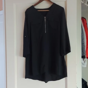 Svart klänning med dragkedja - Säljer en stilren svart klänning med dragkedja framtill. Den har trekvartsärmar och en lös passform, perfekt för både vardag och fest. Klänningen är enkel men elegant, och kan lätt stylas upp eller ner beroende på tillfälle.