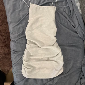 Glittrig axelbandslös klänning - Säljer en superfin glittrig klänning i silver. Den är axelbandslös och har en tight passform som verkligen framhäver figuren. Perfekt för fest eller nyår! ✨