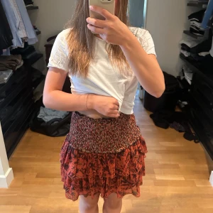 Röd blommig kjol med volang - Säljer en superfin röd kjol med blommigt mönster och volangdetaljer. Den har en elastisk midja som gör den bekväm och lätt att bära. 