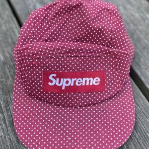 Keps med Supreme märke - Vinröd prickig bomullskeps med Supreme märke fram. Svart spänne bak. 