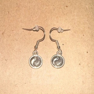 Silverfärgade yin-yang örhängen - Säljer ett par snygga silverfärgade örhängen med yin-yang motiv. De är små och lätta, perfekta för både vardag och fest. Örhängena har en krok för enkel användning. Passar till alla outfits och ger en touch av balans och stil.