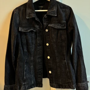 Svart jeansjacka från Lindex - Säljer en  svart/gråmelerad figursydd jeansjacka från Lindex i storlek S. Den har  knappar framtill och två bröstfickor. Perfekt för hösten. Jackan är nästintill oanvänd. Köpt för 699
