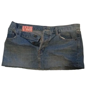 Jeanskjol - Säljer en cool jeanskjol i blå denim med en söt gul rosett på baksidan. Kjolen har en klassisk femficksdesign och är perfekt för vardagsbruk. Den är i bra skick. Storlek står inte men är s-m och den passad