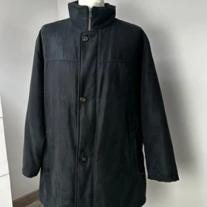 Svart kappa från Bugatti - Säljer en stilren svart kappa från Bugatti. Den är långärmad och har knappar framtill. Jackan är tillverkad i 100% polyester och har ett elegant mönstrat foder. Perfekt för höst och vinter, håller dig varm och snygg! 🖤