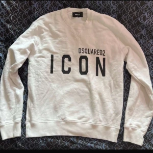 Vit sweatshirt från Dsquared2 - Säljer en stilren vit sweatshirt från Dsquared2 med texten 'ICON' tryckt i svart på framsidan. Tröjan har långa ärmar och en klassisk rund halsringning. Perfekt för en avslappnad och trendig look. Äkta 
