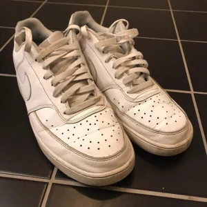 Vita Nike Air Force sneakers - Säljer ett par klassiska vita Nike Air Force sneakers. Skorna har en stilren design med perforerade detaljer på tån och snörning framtill. Perfekta för en avslappnad stil.