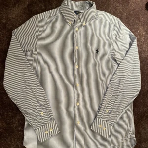 Randig skjorta från Ralph Lauren - Riktigt stilig vit och blå randig polo Ralph lauren skjorta. Storleken är 16 år och är använd ett fåtal gånger. Kom privat vid minsta lilla fundering. 