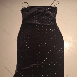 Svart glittrig klänning från H&M - Snygg svart klänning från H&M med glittriga detaljer. Den har smala axelband och en figurnära passform som ger en elegant look. Perfekt för en kväll ute eller en speciell tillställning.