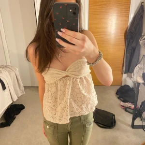 Beige axelbandslös topp med spetsdetaljer - Säljer en söt beige axelbandslös topp med spetsdetaljer och ett twistat mönster upptill. Perfekt för varma sommardagar eller en utekväll. Toppen har ett blommigt mönster och är luftig och bekväm att bära. Står ej storlek men den är antigen s eller xs 💕