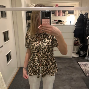 Blus - Säljer en snygg leopardmönstrad blus med knytning framtill. Blusen har korta ärmar och en luftig passform, perfekt för att sticka ut i mängden. 🐆