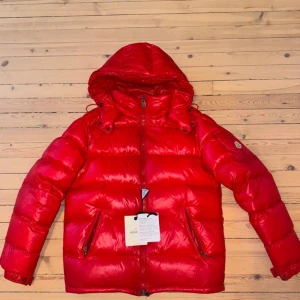 Röd Moncler Maya str 4 - Säljer en snygg röd Moncler Maya. Jackan har en quiltad design och är perfekt för kalla dagar. Den har långa ärmar och praktiska fickor med dragkedja. Storlek 4 som motsvarar L. Tags finns kvar. Nypris 15000kr 