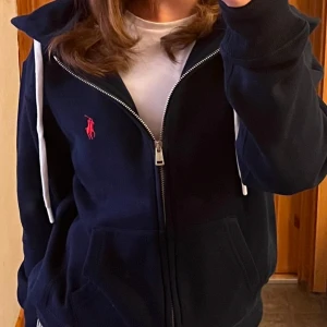 Mörkblå hoodie från Ralph Lauren - Säljer en snygg mörkblå hoodie från Ralph lauren, dock ett pytte litet hål i höger ärm så säljer den mycket billigare än vad ja köpte den för. Andvänd fåtal gånger då jag inte gillade färgen.