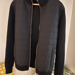 Cardigan - Snygg cardigan med dragkedja och ribbade ärmar. Jackan har en quiltad framsida och en stilren design som passar perfekt för höst och vår. Den har en klassisk passform och är både bekväm och trendig.
