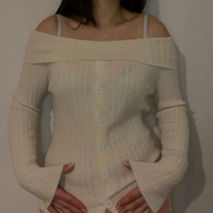 Vit ribbad offshoulder kofta - Säljer en stilren vit ribbad offshoulder kofta med knappar framtill. Koftan har långa ärmar och en elegant design som passar perfekt för både avslappnade och mer uppklädda tillfällen.