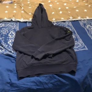 Mörkblå hoodie från Stone Island Junior - Säljer en snygg mörkblå hoodie från Stone Island Junior. Den har en klassisk design med huva och ribbade muddar. Märkets ikoniska logga finns på ärmen. Perfekt för en stilren och bekväm look. Obetydligt använd, priset kan diskuteras!