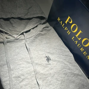 Grå luvtröja från U.S. Polo Assn. - Den funkar för både män och kvinnor. Storlek S/XS på herr och M på kvinnor✨✨ bra kvalité! Älskar den personligen! Kostar nu 400-700kr med samma kvalite som här! 9/10 