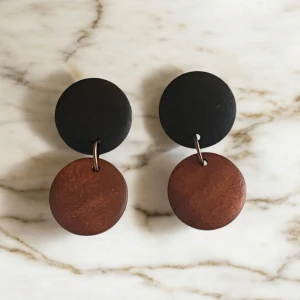 Svart och brunt örhänge i trä - Stilrena örhängen med en modern design. De har en rund svart topp och en rund brun botten, sammanlänkade med en liten metallring. Perfekta för att ge en elegant touch till din outfit.