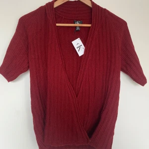 Röd kofta från Calvin Klein - Snygg röd kofta från Calvin Klein i ribbat material. Den har en djup v-ringning och korta ärmar, perfekt för lager-på-lager-stil. Passar utmärkt för både höst och vår. Ett stilrent plagg som ger en trendig touch till din garderob.