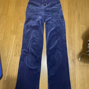 Mörkblå mjukisbyxor från Juicy Couture - Snygga mörkblå mjukisbyxor från Juicy Couture med snörning i midjan och bakfickor med knappar. Perfekta för en avslappnad stil med en touch av lyx. Säljer då jag inte använder dem. Fråga om fler bilder vid önskan💗💕