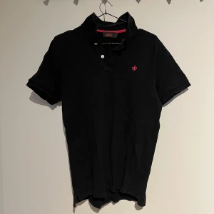 Svart och grå pikétröja från Morris - Två stilrena pikétröjor från Morris i storlek L. En i klassisk svart och en i grått, båda med korta ärmar och en broderad röd detalj på bröstet. Perfekta för en avslappnad men snygg look. Båda två för 350kr.