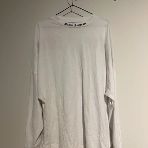 Vit långärmad tröja från Palm Angels - Säljer en stilren vit långärmad tröja från Palm Angels med deras ikoniska logga tryckt i svart på baksidan och vid halsen. Perfekt för en avslappnad och trendig look.