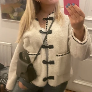 Vit teddyjacka med svarta detaljer - Mysig vit teddyjacka med svarta knappar och kantdetaljer. Jackan har en avslappnad passform och långa ärmar, perfekt för kyligare dagar. Den har en unik design med knappar framtill som ger en stilren look. Storlek 38💕💕💕💕 säljer för att den inte används! Använd 5 gånger 💕Orginal pris 1300, säljer för 800! Märket är object och är slutsåld på hemsidan. Kan tänka mig gå ner i pris! 